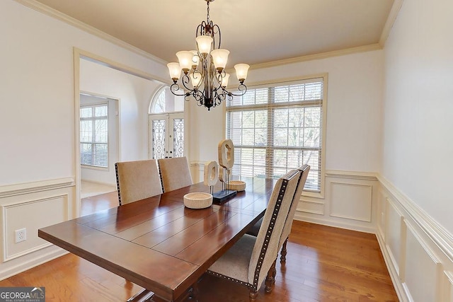 dining room featuring a decorative wall, crown molding, a wainscoted wall, wood finished floors, and a notable chandelier