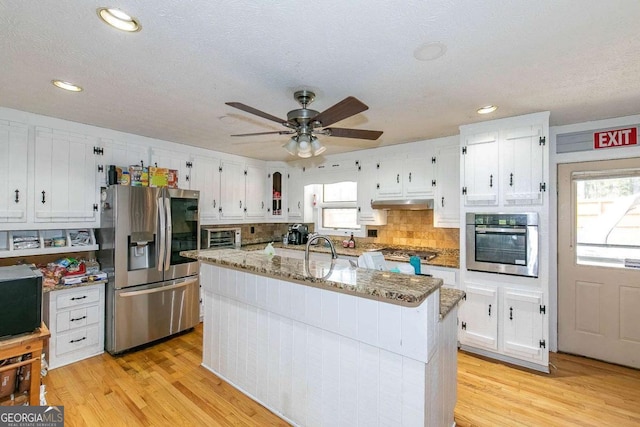 kitchen featuring stainless steel appliances, stone countertops, a center island with sink, and light hardwood / wood-style floors