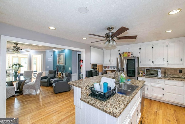 kitchen featuring a kitchen island with sink, sink, light stone countertops, and stainless steel refrigerator with ice dispenser