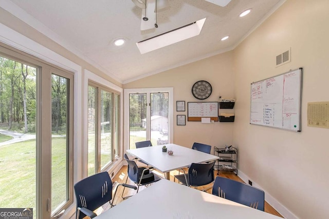 dining space featuring wood-type flooring, ornamental molding, and vaulted ceiling with skylight