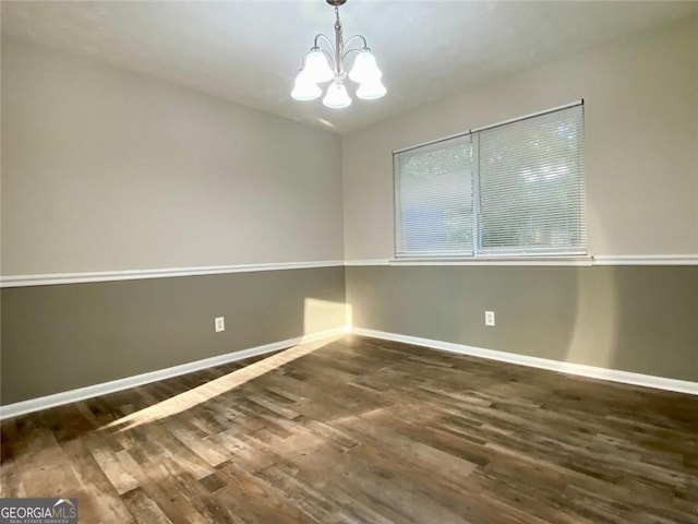 empty room featuring dark wood-type flooring and an inviting chandelier