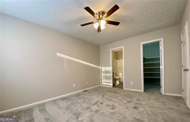 unfurnished bedroom featuring ensuite bath, ceiling fan, carpet, a spacious closet, and a closet