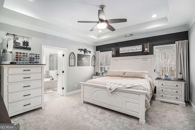 carpeted bedroom featuring crown molding, ensuite bath, a tray ceiling, and ceiling fan