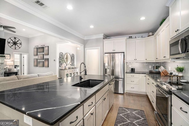 kitchen with sink, dark wood-type flooring, appliances with stainless steel finishes, white cabinets, and a large island with sink