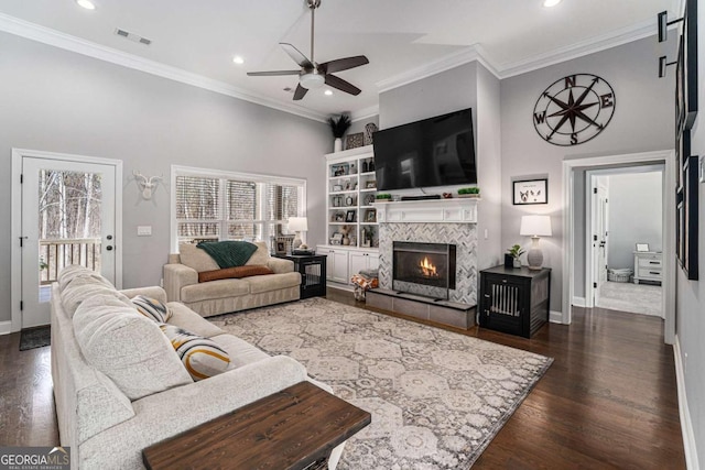 living room featuring a tiled fireplace, crown molding, dark wood-type flooring, and ceiling fan