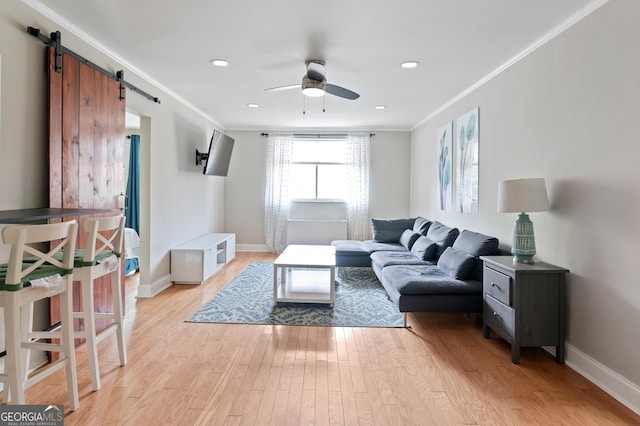 living room with ceiling fan, ornamental molding, a barn door, and light hardwood / wood-style floors