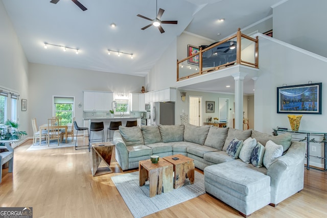 living room featuring ceiling fan, high vaulted ceiling, ornate columns, and light hardwood / wood-style flooring