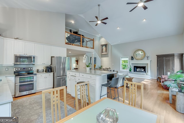 kitchen with light wood-type flooring, high vaulted ceiling, a breakfast bar, appliances with stainless steel finishes, and white cabinets