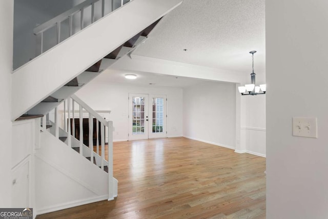 unfurnished living room featuring an inviting chandelier, wood-type flooring, french doors, and a textured ceiling