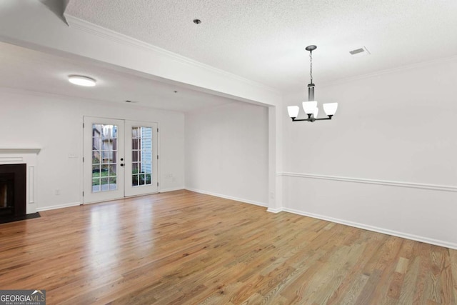 interior space with light hardwood / wood-style flooring, a notable chandelier, ornamental molding, a textured ceiling, and french doors