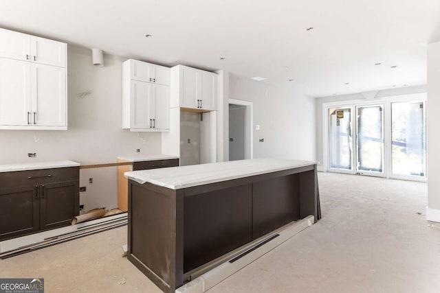 kitchen featuring white cabinetry, dark brown cabinets, light stone countertops, and a kitchen island