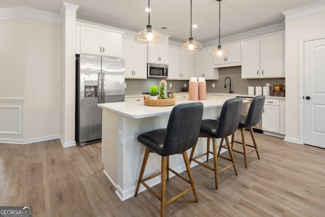 kitchen with appliances with stainless steel finishes, decorative light fixtures, white cabinetry, an island with sink, and ornamental molding