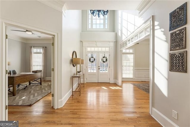 foyer entrance with a towering ceiling, ornamental molding, and light wood-type flooring