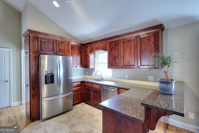 kitchen featuring sink, vaulted ceiling, appliances with stainless steel finishes, kitchen peninsula, and dark stone counters