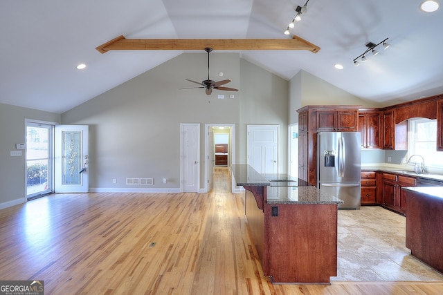 kitchen with sink, stainless steel fridge, dark stone countertops, a kitchen breakfast bar, and light hardwood / wood-style floors