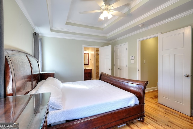 bedroom with crown molding, ensuite bathroom, a raised ceiling, and light hardwood / wood-style floors