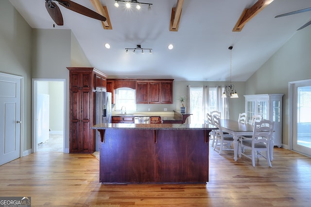 kitchen featuring a breakfast bar, hanging light fixtures, appliances with stainless steel finishes, beamed ceiling, and light hardwood / wood-style floors