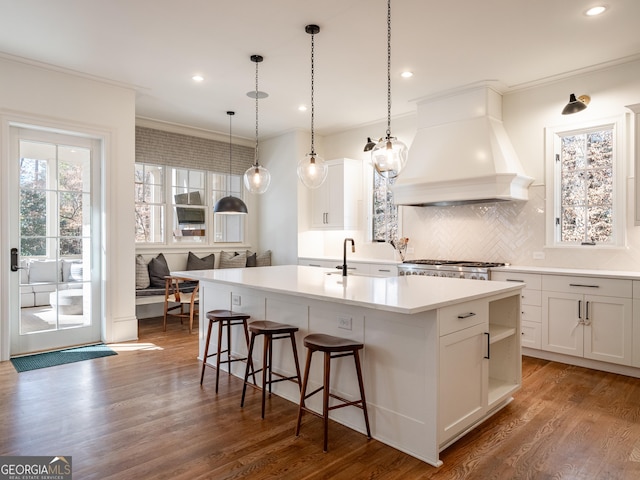 kitchen featuring ornamental molding, custom range hood, hardwood / wood-style flooring, a kitchen island with sink, and white cabinets