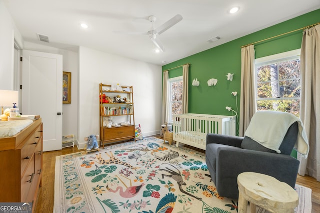 bedroom with a crib, ceiling fan, and light hardwood / wood-style floors