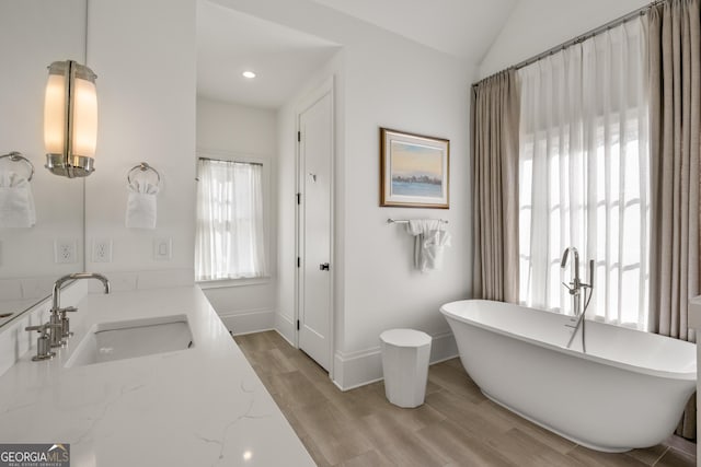 bathroom featuring hardwood / wood-style flooring, a bathing tub, vaulted ceiling, and vanity