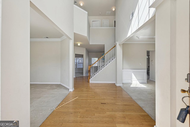 foyer entrance featuring crown molding, a towering ceiling, and light hardwood / wood-style floors