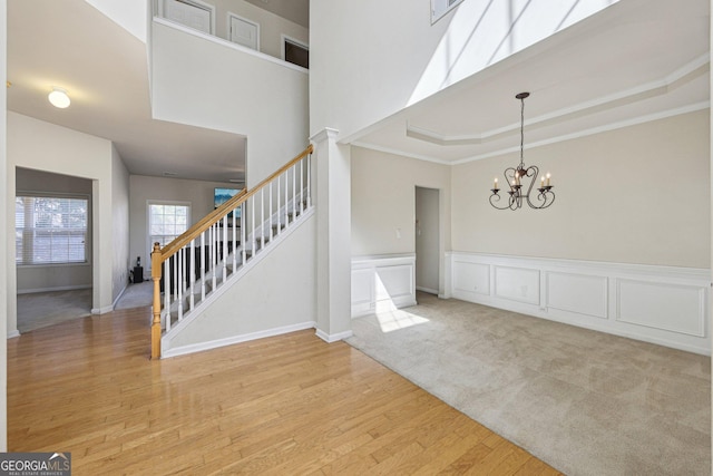 entryway featuring crown molding, an inviting chandelier, light wood-type flooring, a raised ceiling, and a towering ceiling