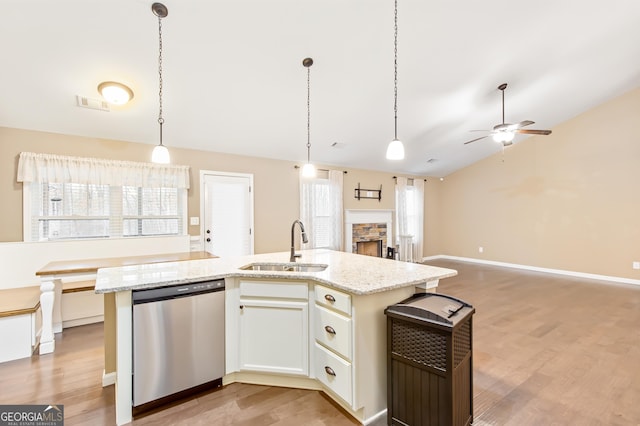 kitchen featuring dishwasher, hanging light fixtures, light stone counters, white cabinets, and a center island with sink