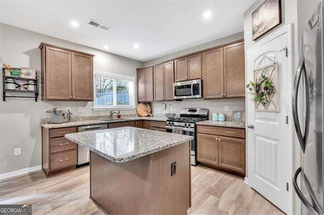 kitchen featuring sink, a center island, stainless steel appliances, light stone countertops, and light hardwood / wood-style floors