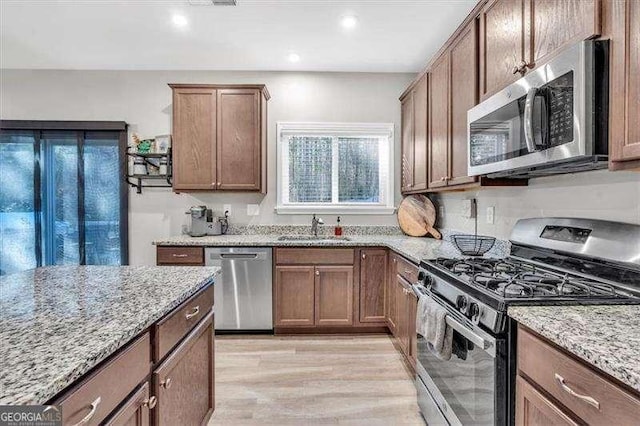 kitchen with light stone countertops, appliances with stainless steel finishes, sink, and light hardwood / wood-style flooring