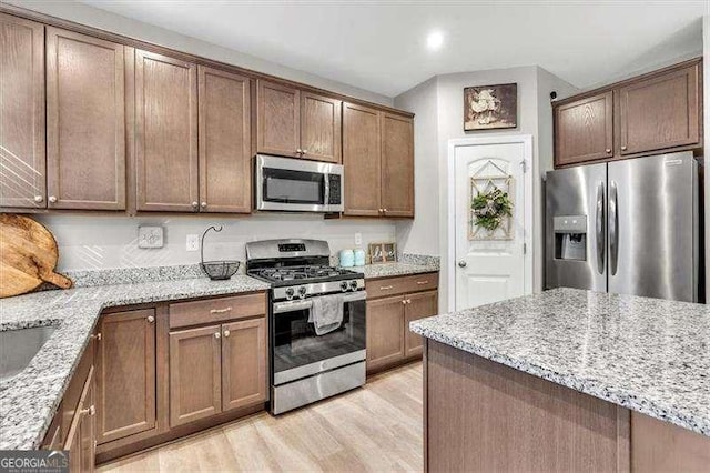 kitchen featuring appliances with stainless steel finishes, light stone countertops, and light wood-type flooring