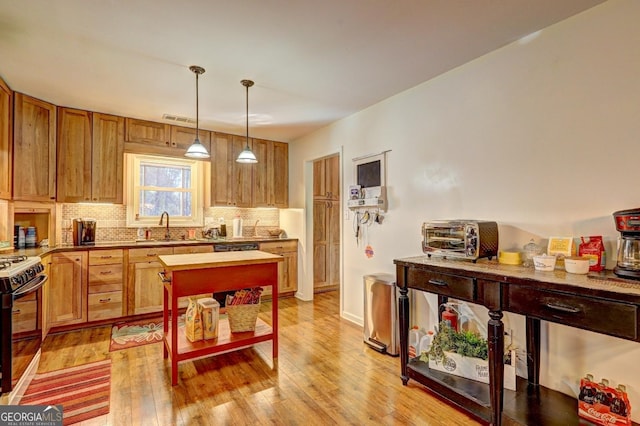 kitchen with range with gas cooktop, tasteful backsplash, sink, hanging light fixtures, and light hardwood / wood-style floors