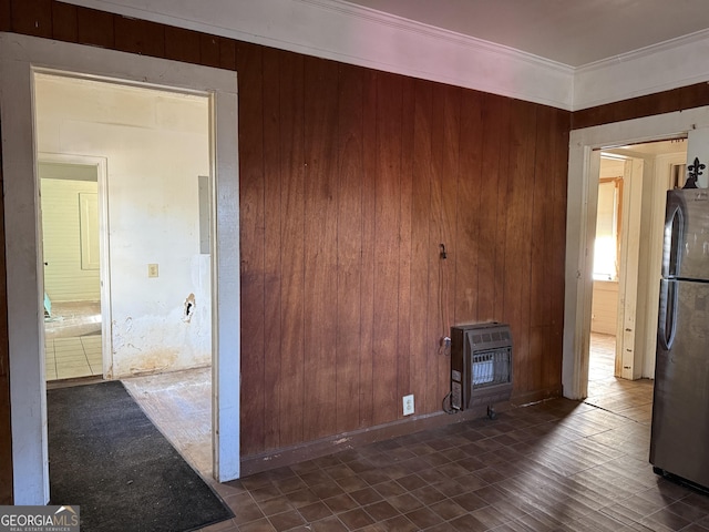 unfurnished living room featuring heating unit, wooden walls, ornamental molding, and a wood stove