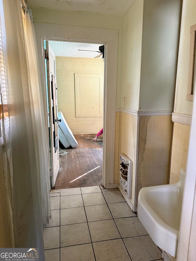 corridor featuring heating unit, light tile patterned floors, and tile walls