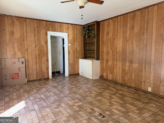 empty room featuring ceiling fan and wooden walls