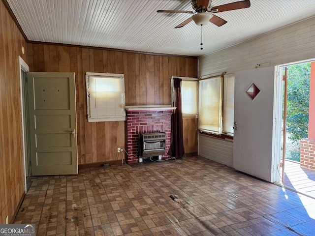 unfurnished living room with ceiling fan, wooden walls, and heating unit