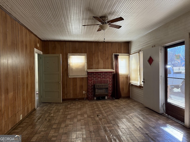 unfurnished living room with ceiling fan, a brick fireplace, and wood walls