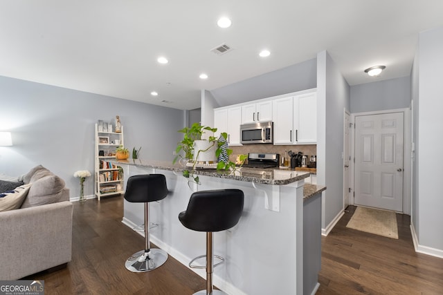 kitchen with appliances with stainless steel finishes, tasteful backsplash, white cabinetry, a breakfast bar area, and dark stone countertops