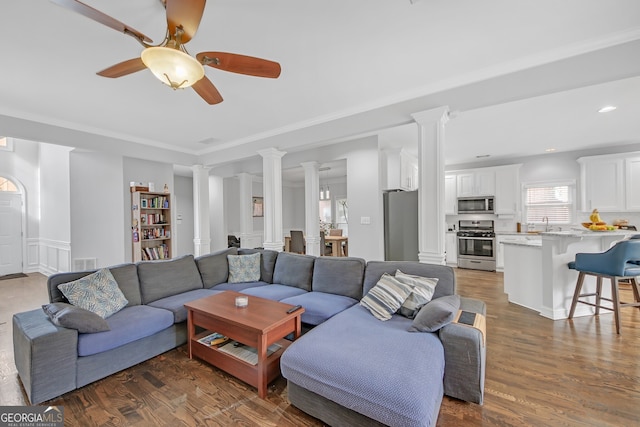 living room with sink, dark wood-type flooring, ceiling fan, decorative columns, and ornamental molding