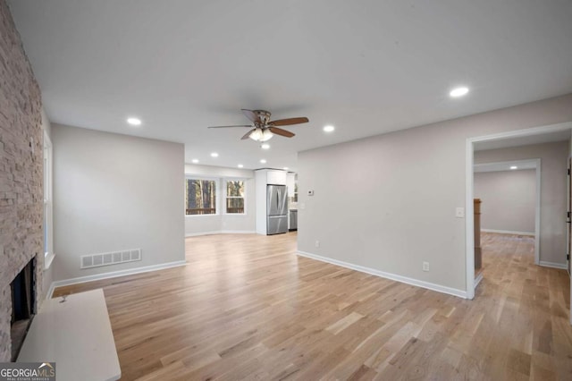 unfurnished living room with a stone fireplace, light hardwood / wood-style floors, and ceiling fan