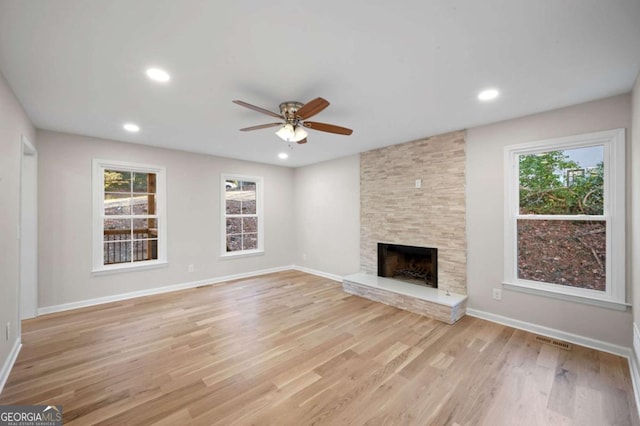 unfurnished living room with a large fireplace, ceiling fan, and light wood-type flooring