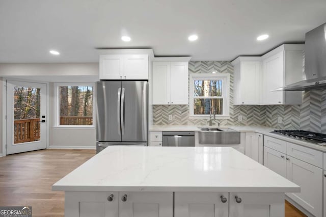 kitchen with light stone counters, wall chimney exhaust hood, stainless steel appliances, and sink