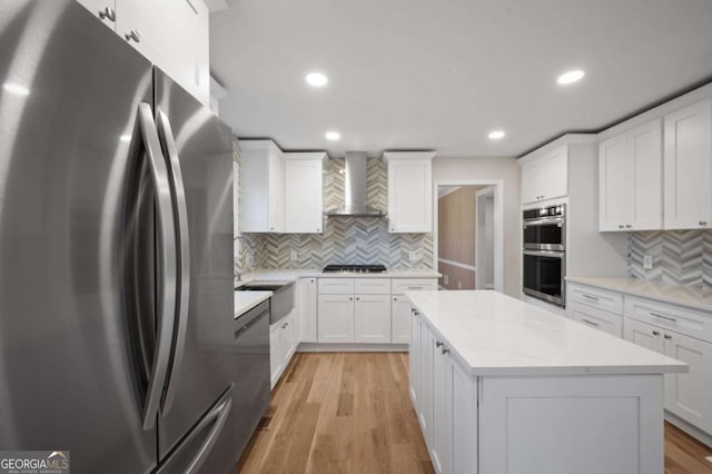 kitchen with wall chimney range hood, stainless steel appliances, white cabinets, and a kitchen island