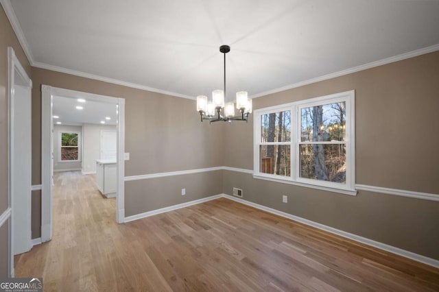 spare room with a notable chandelier, ornamental molding, and light hardwood / wood-style floors