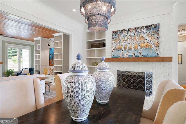 dining area with crown molding, a brick fireplace, a chandelier, and built in shelves