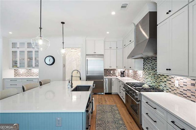 kitchen featuring sink, premium appliances, an island with sink, pendant lighting, and wall chimney range hood