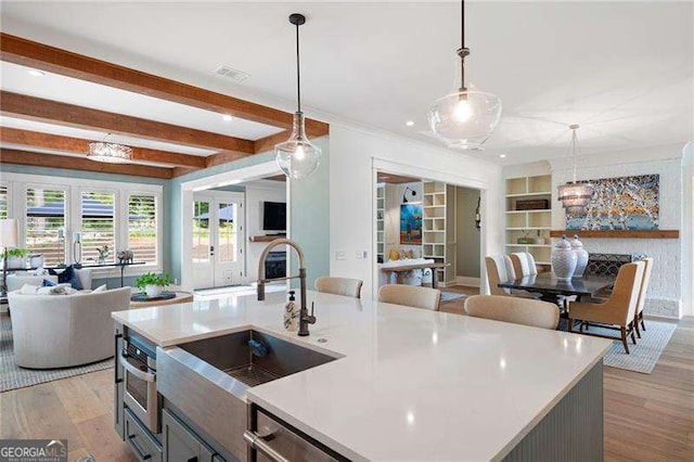 kitchen with hanging light fixtures, a kitchen island with sink, sink, and light hardwood / wood-style flooring