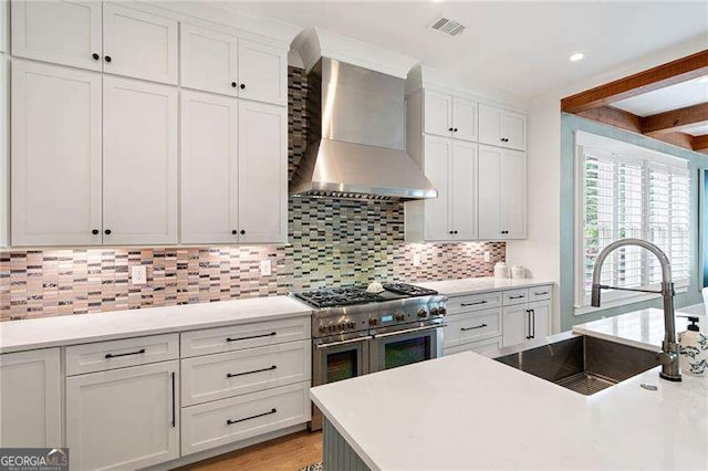 kitchen with white cabinetry, double oven range, sink, and wall chimney exhaust hood