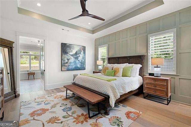 bedroom featuring ceiling fan, ornamental molding, a raised ceiling, and light wood-type flooring