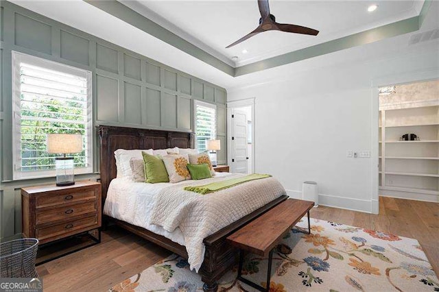 bedroom featuring a raised ceiling, ornamental molding, ceiling fan, and light hardwood / wood-style flooring