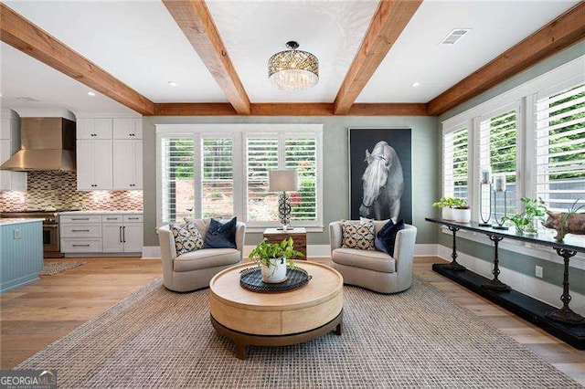 living room with beam ceiling, a wealth of natural light, a notable chandelier, and light hardwood / wood-style floors